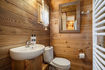 Cozy cabin bathroom with warm wood paneling, a white ceramic sink and toilet, and a wooden-framed mirror.