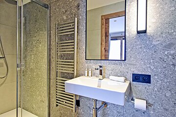 Modern bathroom with grey patterned tiles, a glass shower, heated towel rail, white sink, mirror, and wall lighting.
