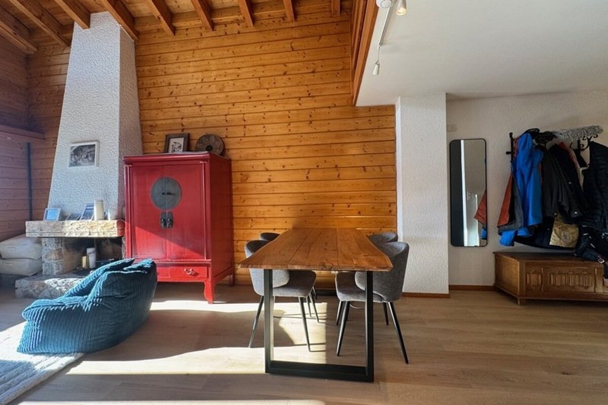 Cozy cabin interior with a wooden dining table, grey chairs, a striking red cabinet, a fireplace, and a large blue beanbag.