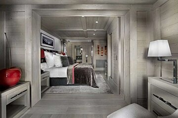 A chic, wood-paneled bedroom in neutral tones, featuring a large bed, elegant furnishings, and a cozy, modern chalet-style design.