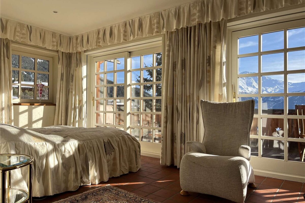 A bedroom with a bed and a chair with a view of the mountains