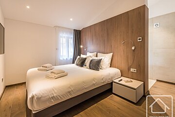 Modern bedroom with wood accent wall, white bedding, folded towels, nightstand, and an adjacent bathroom area.