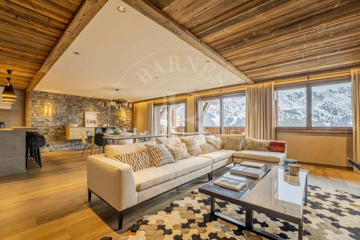 Chic open-plan chalet living/dining room with stunning snowy mountain views, warm wood ceilings, stone walls, and modern decor.