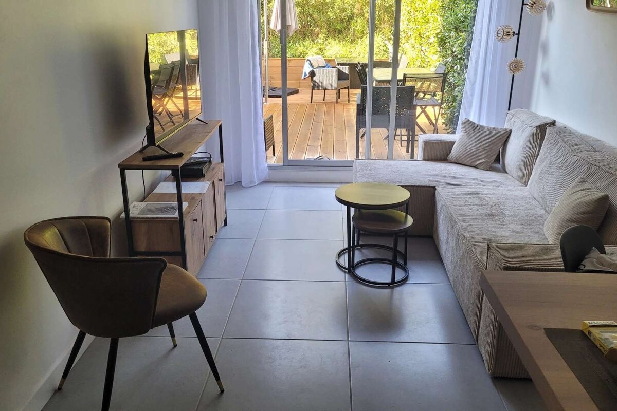 Cozy living room featuring a TV, beige L-shaped sofa, nesting tables, and a large sliding door leading to an outdoor wooden deck.