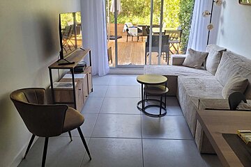 Cozy living room featuring a TV, beige L-shaped sofa, nesting tables, and a large sliding door leading to an outdoor wooden deck.