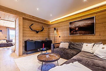 Cozy wooden chalet living room with a large grey sectional sofa, round coffee tables, and a framed deer picture on the wall.