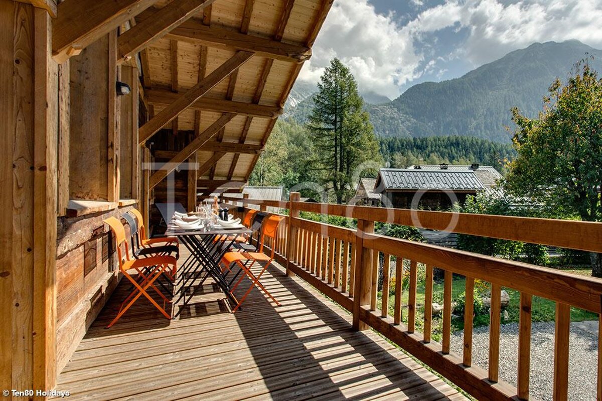 A wooden deck with a table and chairs and mountains in the background