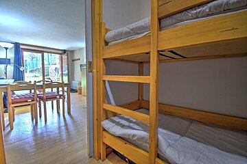 Bunk beds flank a doorway opening to a dining area with wood floors and sliding glass doors leading to an outdoor space.