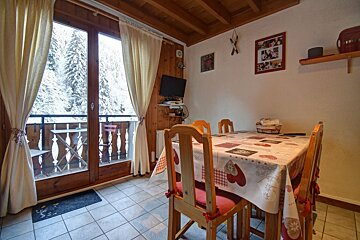 A cozy cabin dining room with wooden chairs and a table, next to glass doors opening to a snowy forest view.