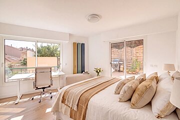 A bright bedroom featuring neutral bedding, a desk with an office chair by a large window, and glass doors opening to a patio.
