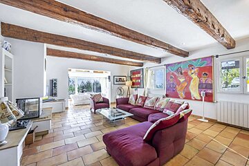 A spacious living room with exposed wooden beams, terracotta tile flooring, a large red sectional sofa, and a vibrant painting, filled with natural light.