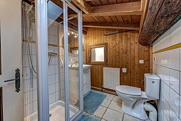 Rustic bathroom with wood walls/ceiling, tiled floor, glass shower, toilet, and sink.