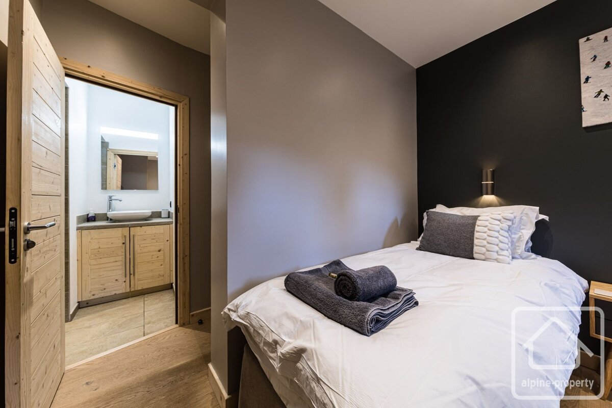 A bedroom with a white and gray single bed next to an open bathroom door.