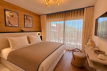 A cozy, modern bedroom featuring a wood-paneled wall, a large bed, a small vanity desk, and large sliding doors leading to a balcony.