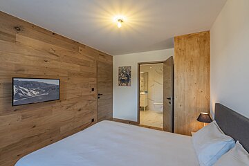 A bedroom with a large bed and a television on the wall
