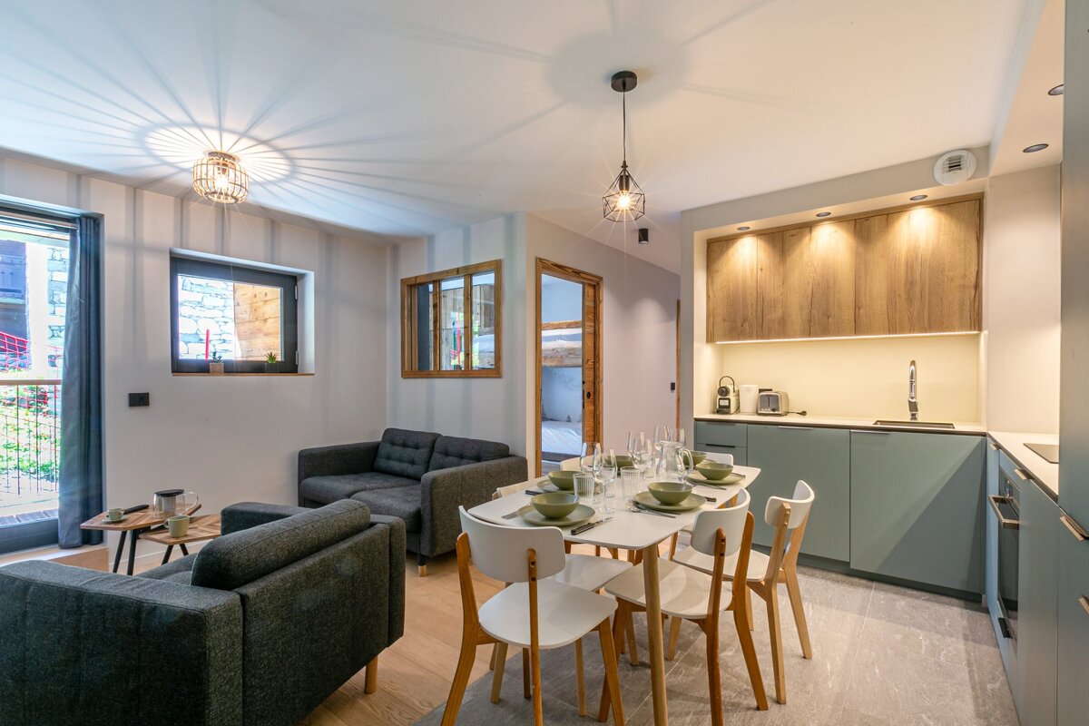Modern open-plan apartment featuring a cozy living area with grey sofas, a dining set, and a sleek green and wood kitchen.