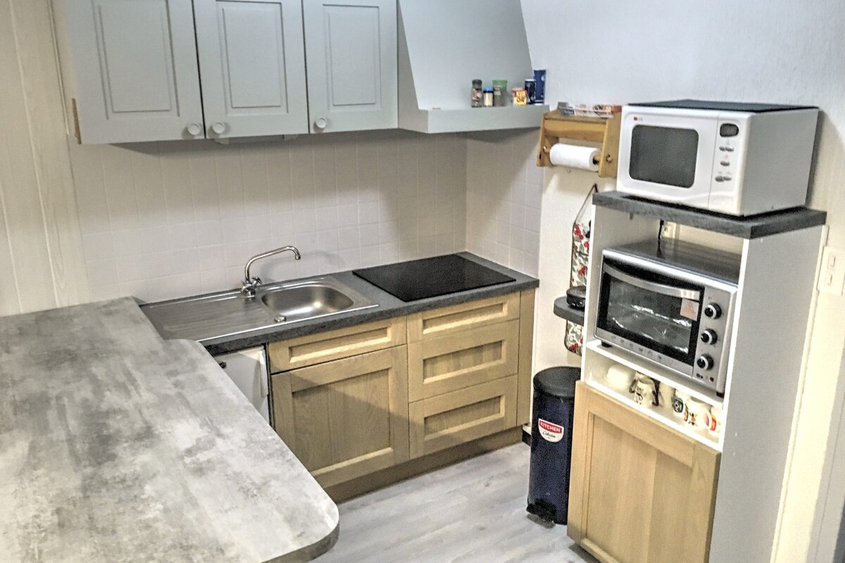 A small kitchen with a microwave and a trash can