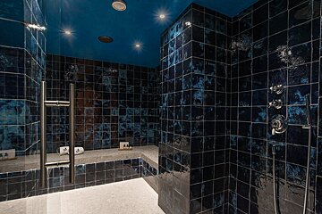 A modern walk-in shower room with dark blue textured tiles, a bright blue ceiling with spotlights, and chrome fixtures, including a glass door.