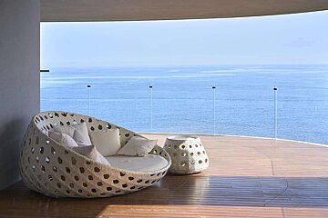 A wicker couch sits on a balcony overlooking the ocean