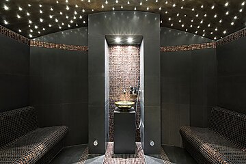Dark, luxurious steam room or spa with a starry ceiling, mosaic benches, and a central water feature.