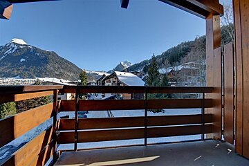 Wooden balcony view of a snowy alpine village with chalets and mountains under a clear blue sky.