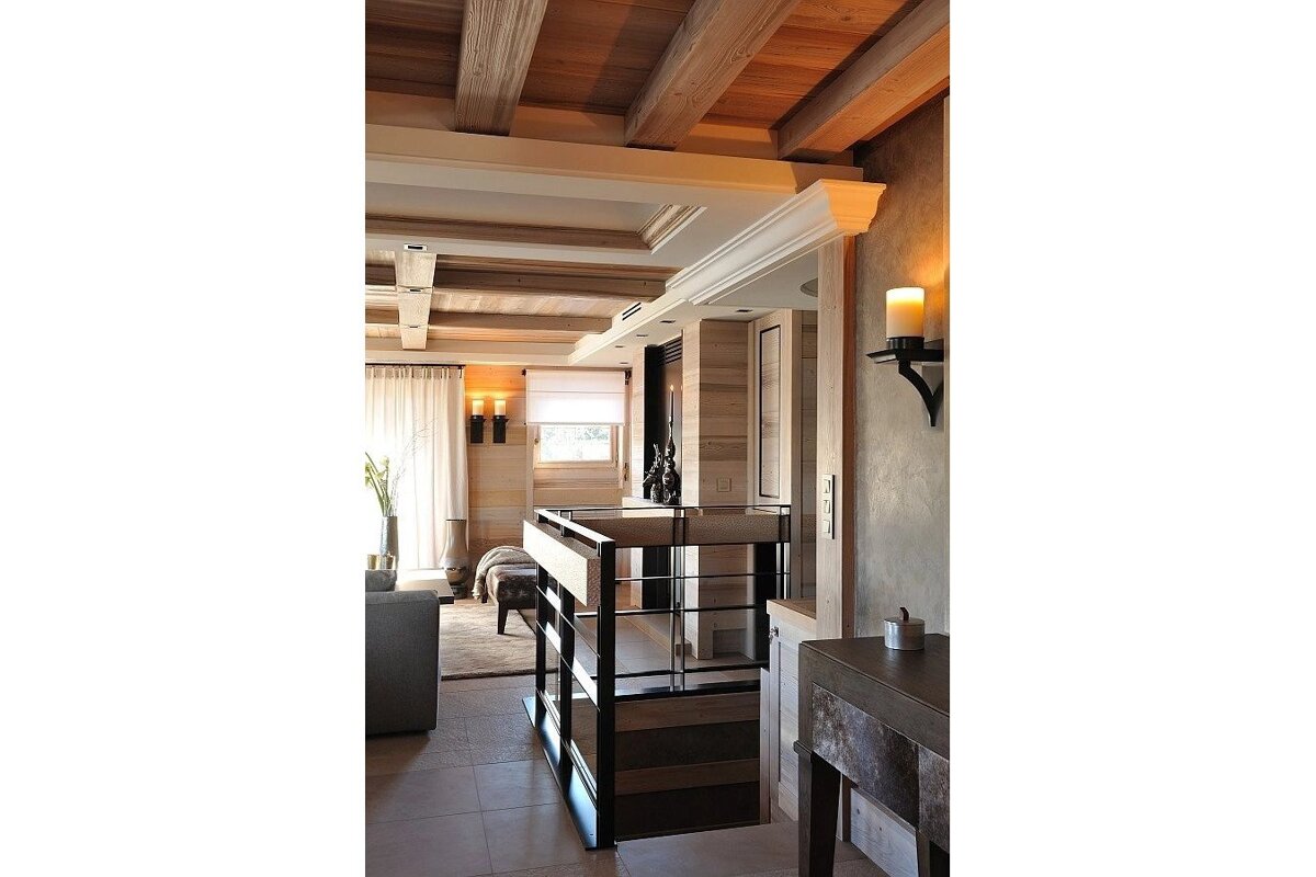 A cozy, rustic modern interior with exposed wood beams, paneling, and warm lighting from sconces and candles. A stylish staircase leads downstairs.