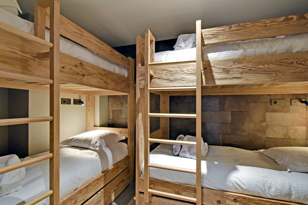 A wooden bunk bed with white sheets and a ladder