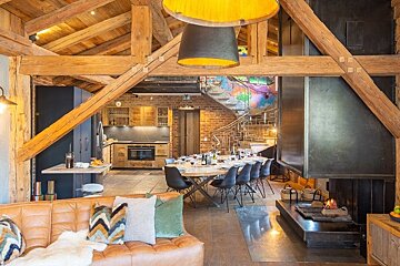 A cozy, modern rustic cabin interior with exposed wooden beams, a leather sofa, a large fireplace, and a dining area.