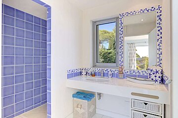 Bright blue & white bathroom with tiled shower, vanity, and window. Blue mosaic and starfish decor create a fresh, coastal vibe.
