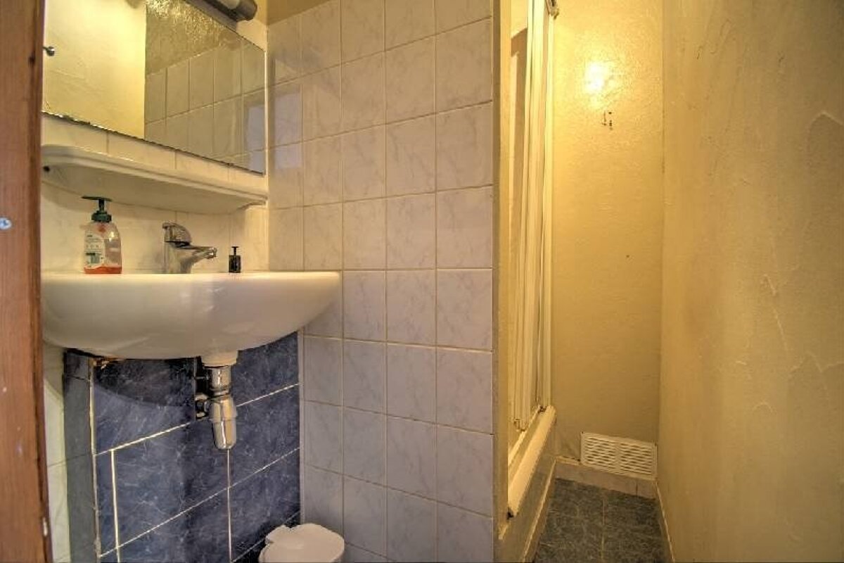 A compact bathroom featuring a white wall-mounted sink with blue tiles below, next to a narrow tiled shower stall.