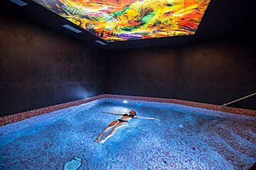 A woman is floating in a pool with a colorful ceiling