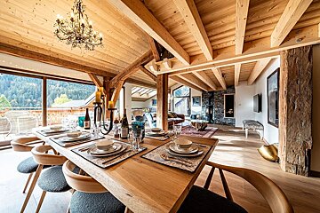 A spacious, rustic-chic dining room with a set table, wood beams, and a chandelier, offering stunning mountain views through large windows.