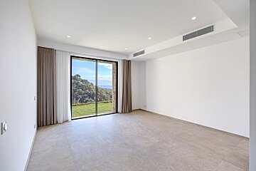Bright, empty modern room with white walls, gray tiled floor, and a large window looking out to green hills and blue sea.