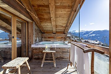 A wooden balcony with a hot tub and mountains in the background