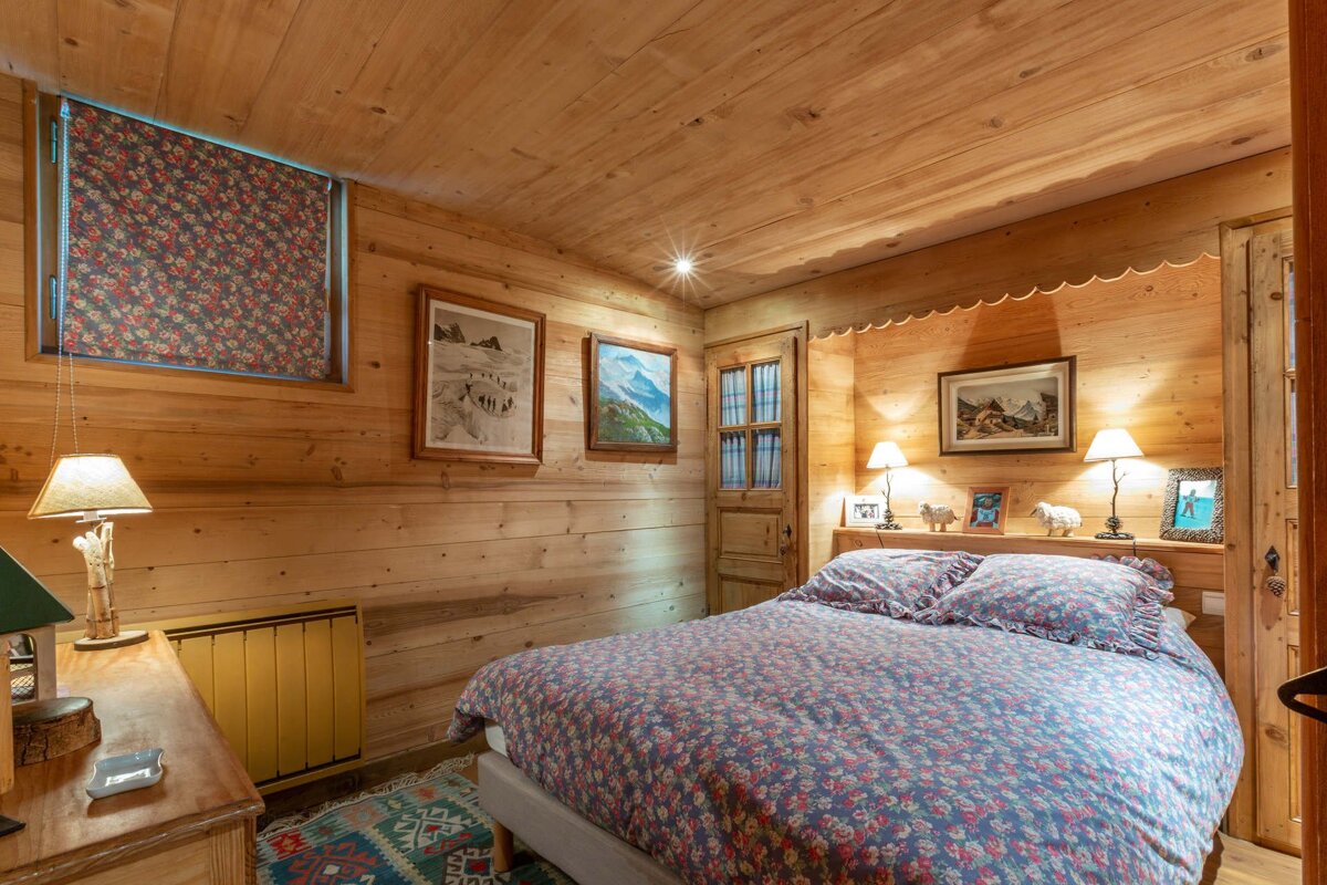 Cozy rustic cabin bedroom with wood-paneled walls and ceiling, a bed with floral bedding, and warm bedside lamps.