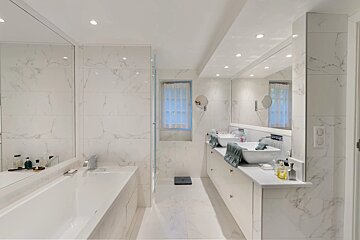 Modern, luxurious white marble bathroom with a large tub, double vanity, and expansive mirrors, creating a bright and spacious feel.