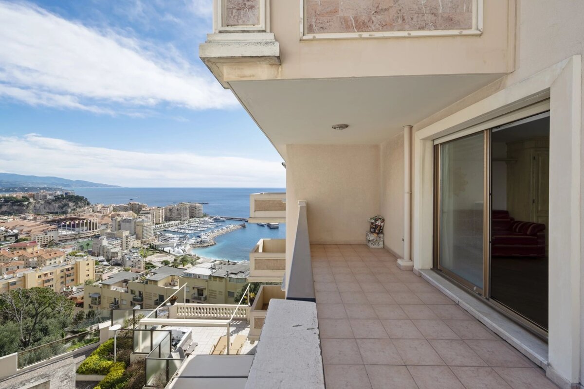 A tiled balcony overlooks a coastal city, harbor, and sea under a cloudy sky.