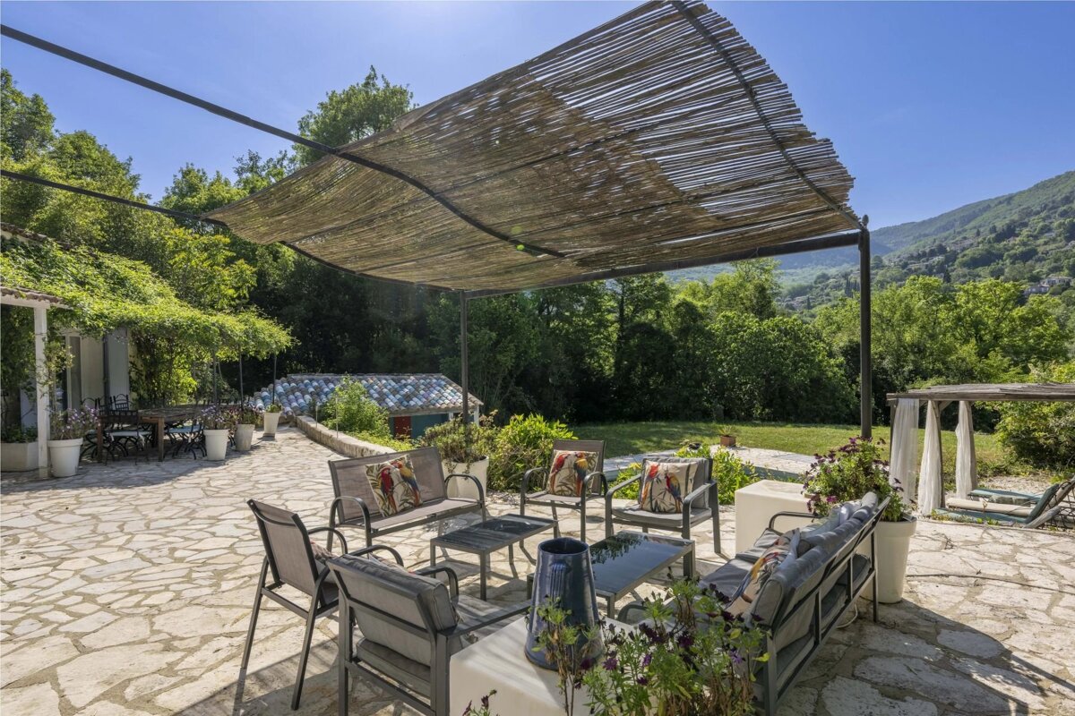 Sunny outdoor patio with comfortable seating under a bamboo pergola, overlooking green hills and lush vegetation.