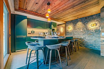Modern kitchen featuring teal cabinets, a rustic wood ceiling, a stone accent wall, and a large dining island with stools.