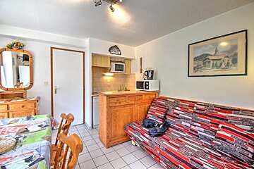 Cozy studio apartment featuring a compact kitchen, patterned pull-out sofa bed, dining table, mirror, and tiled floor.