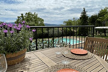 A scenic outdoor table with potted lavender, wine glasses, and plates, overlooking a swimming pool, lush greenery, and distant mountains.