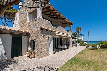 A white house with a stone facade sits next to the ocean