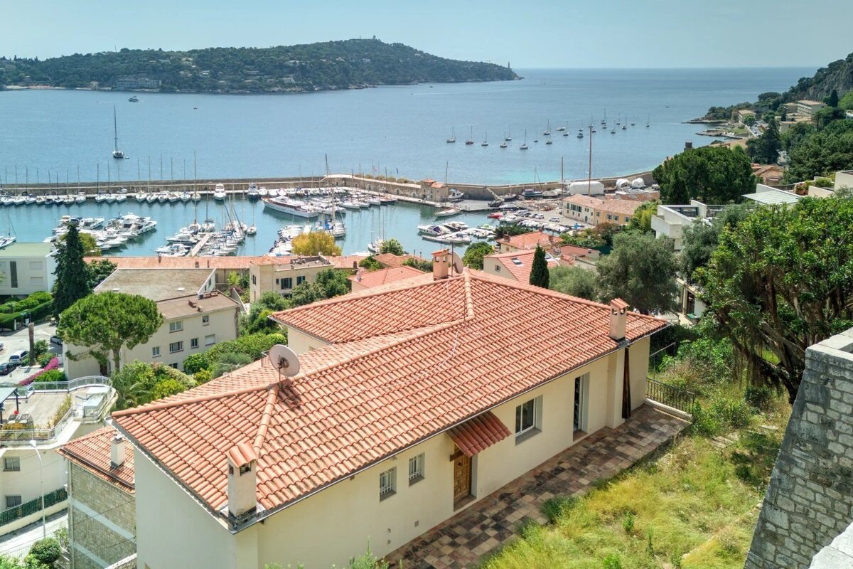 Scenic view overlooking a coastal town with red-roofed buildings, a busy marina filled with boats, and a distant peninsula.