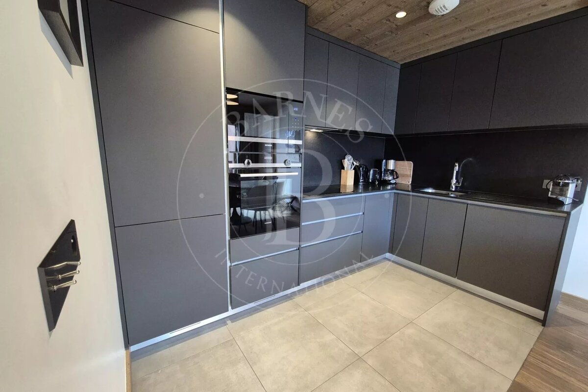 A sleek, modern kitchen featuring dark gray cabinets, built-in appliances, light tile flooring, and a rustic wood ceiling.