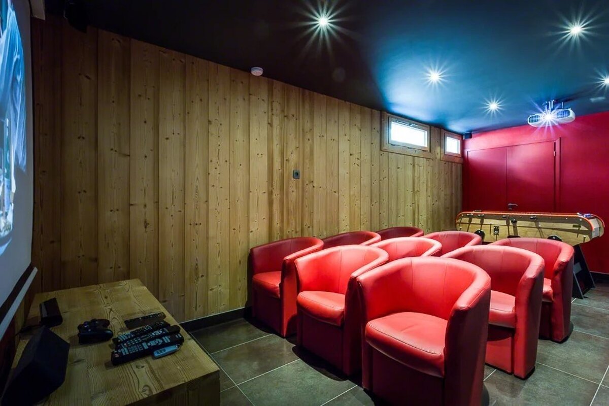 Home theater room with wood-paneled walls, red armchairs, a projection screen, and a foosball table.