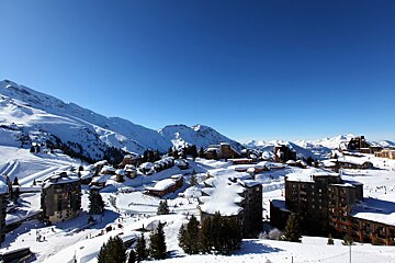 A bustling snowy ski resort town nestled amidst majestic snow-covered mountains under a brilliant clear blue sky.