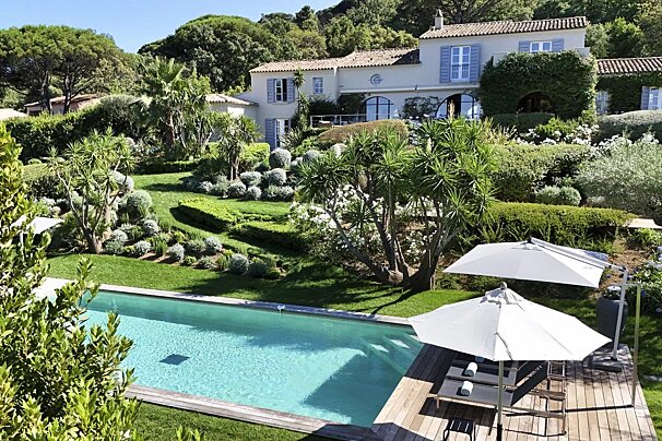 A luxury villa with a swimming pool and sun loungers set in beautiful lush, landscaped gardens.