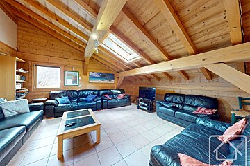 A cozy wooden attic living room with black leather sofas, a coffee table, tiled floor, exposed beams, a skylight, and a window.