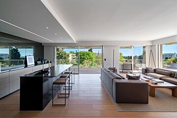 A modern open-plan living room and kitchen with sleek black island, wooden floors, and large windows opening to a balcony.