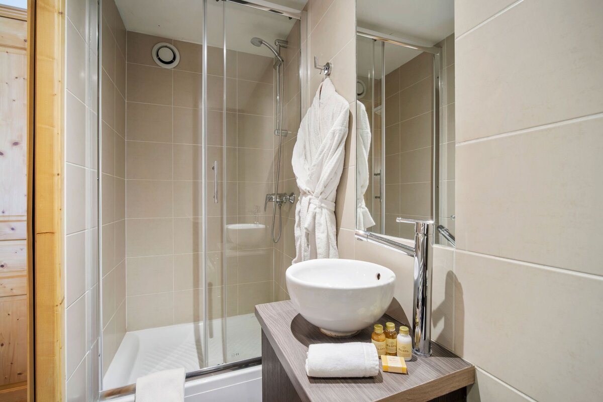 Modern bathroom featuring a glass shower stall, a white vessel sink on a wooden vanity, a hanging bathrobe, and toiletries.